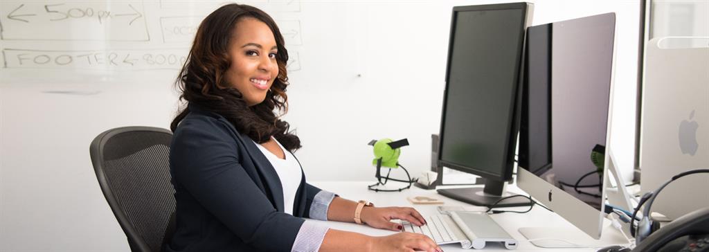 Receptionist at desk in front of two monitors smiling at the camera